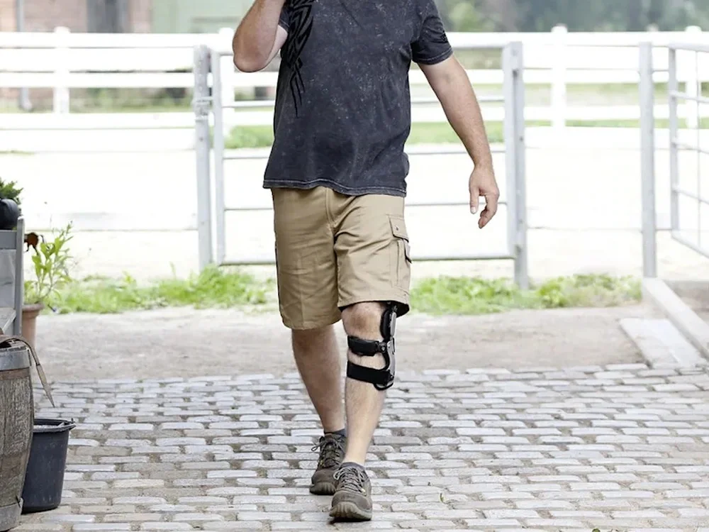 Diz osteoartriti unloader ortezi: Dizinde ortezle çiftlik avlusunda çalışan kişi